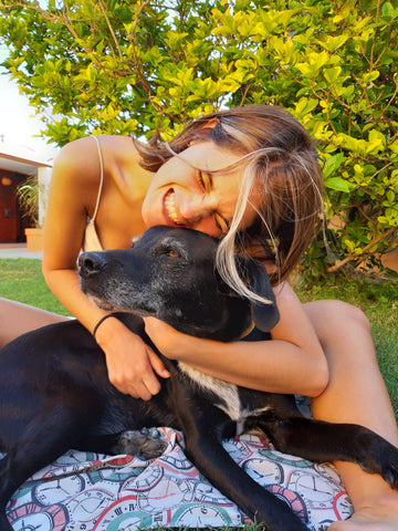 A cute black dog being hugged by his owner outside in the sun